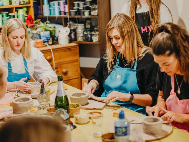 Three women in aprons at a clay and sip class